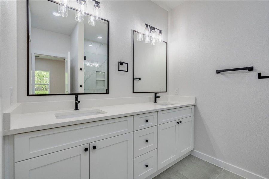 Double vanities with sleek black fixtures and framed mirrors elevate this pristine and modern bathroom space.