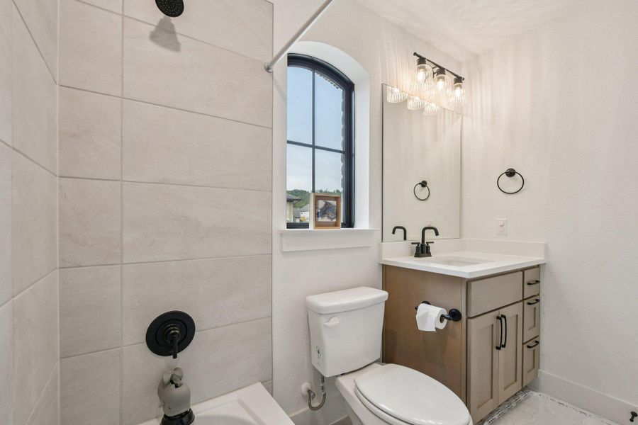 Bathroom featuring a tiled shower, a vanity with a white countertop and dark fixtures, and an arched window Bathroom featuring a tiled shower, a vanity with a white countertop and dark fixtures, and an arched window