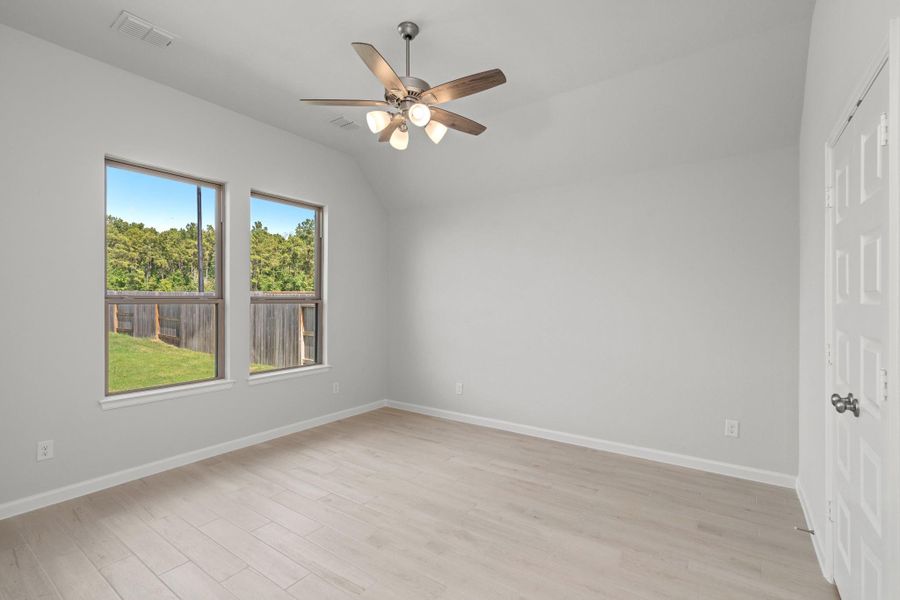 Primary bedroom with large windows overlooking the fenced backyard.