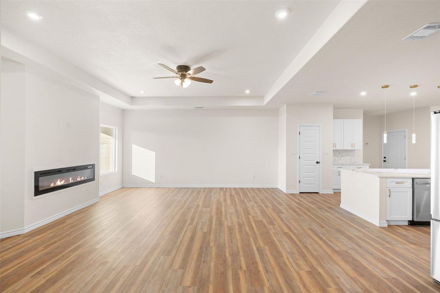Unfurnished living room with a glass covered fireplace, light wood-style flooring, a raised ceiling, ceiling fan, and recessed lighting Unfurnished living room with a glass covered fireplace, light wood-style flooring, a raised ceiling, ceiling fan, and recessed lighting