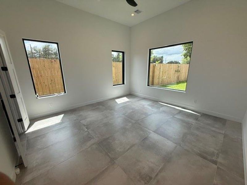 Bright and spacious Primary bedroom on the first floor with large windows offering ample natural light and views of the backyard pool, featuring sleek tile flooring and high ceilings.