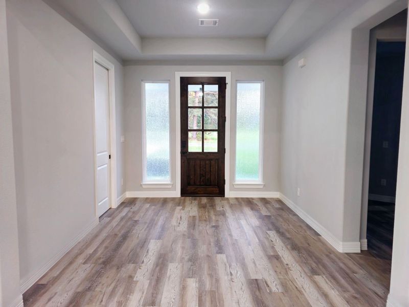 Entryway features a wooden front door with glass panes, flanked by tall windows.