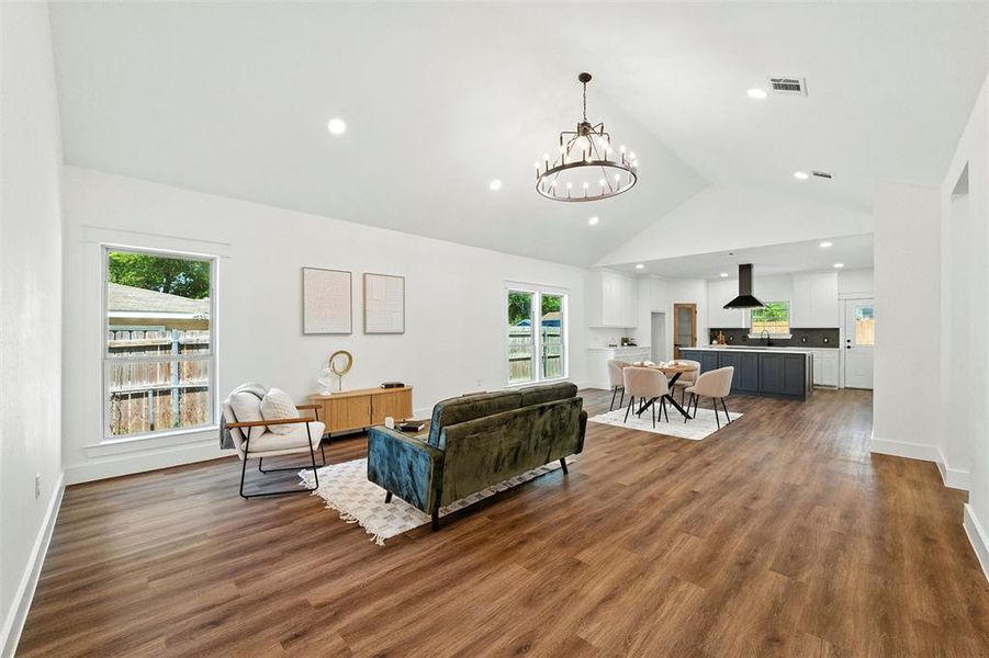 Living area featuring a chandelier, high vaulted ceiling, plenty of natural light, wood finished floors, and recessed lighting