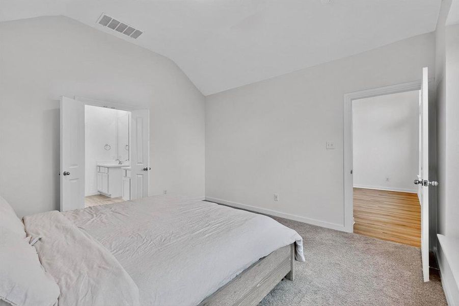 Bedroom featuring vaulted ceiling, light colored carpet, and ensuite bath Bedroom featuring vaulted ceiling, light colored carpet, and ensuite bath