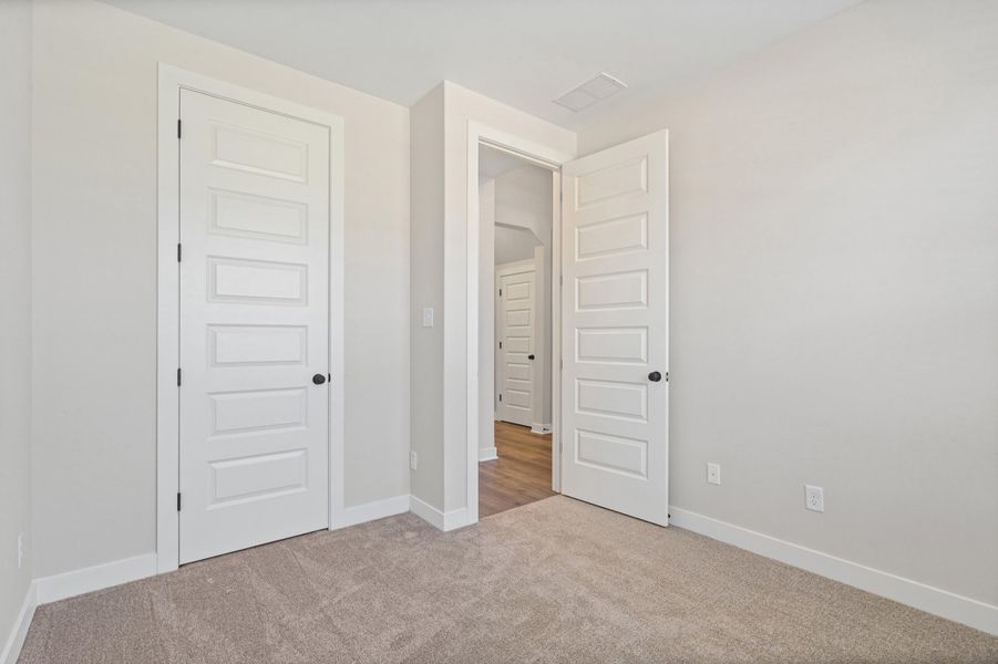 Carpeted room with light gray walls, white baseboards, and a white five-panel interior door with a black knob Carpeted room with light gray walls, white baseboards, and a white five-panel interior door with a black knob