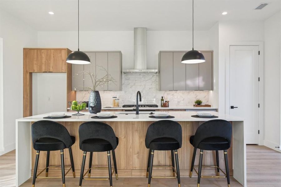 Kitchen with backsplash, a center island with sink, a kitchen bar, decorative light fixtures, and wall chimney exhaust hood