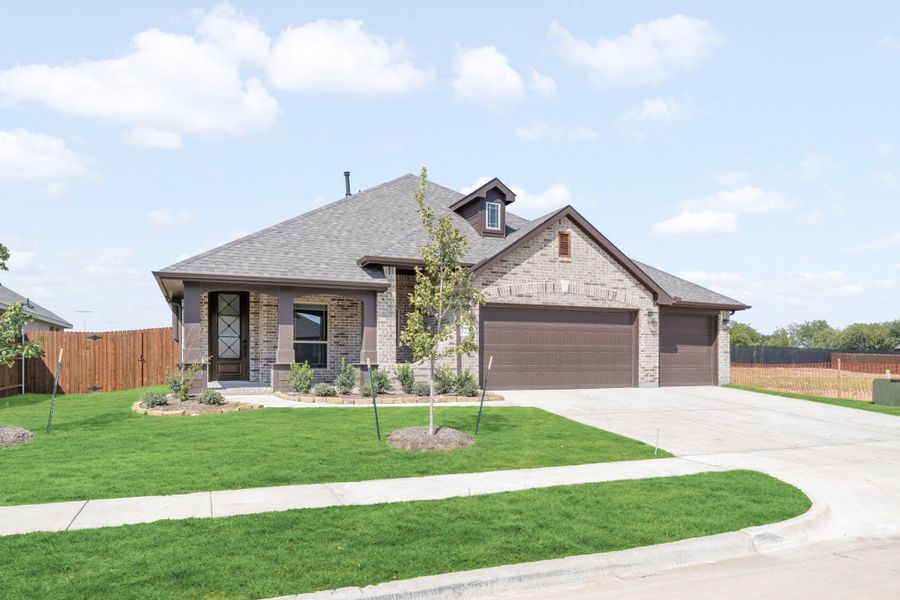 Single-story brick home with two-car garage, gray roof, and landscaped front yard with young tree.