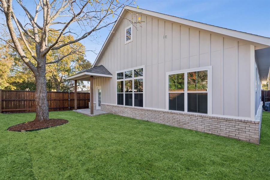 Back of house with board and batten siding, a patio, brick siding, and roof with shingles