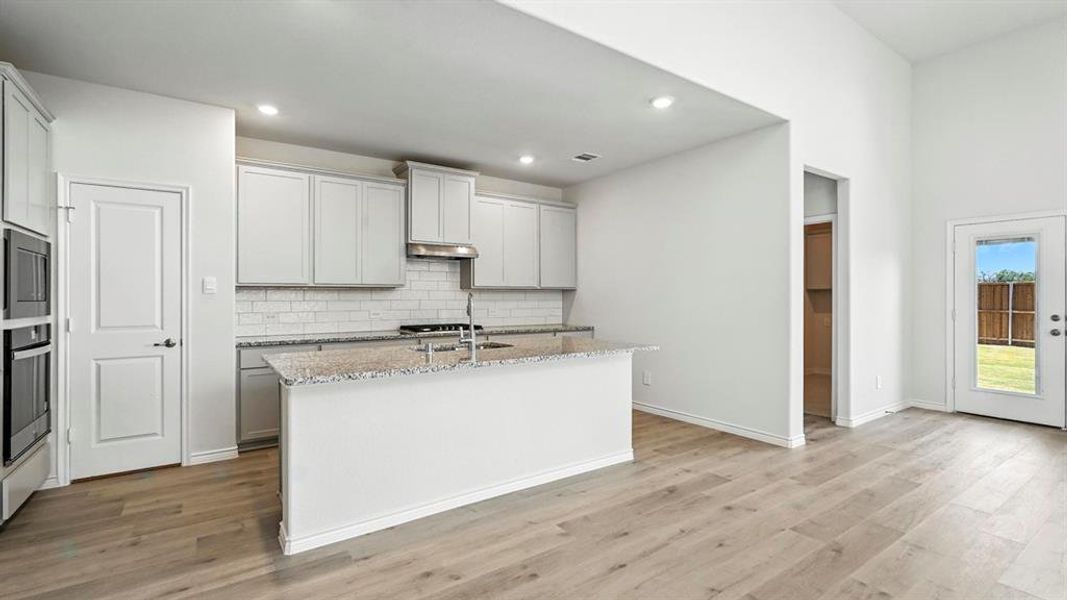 Open-concept kitchen and living area featuring wood-finish flooring, recessed lighting, and a vaulted ceiling