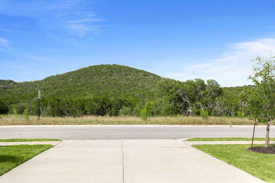 A spacious concrete driveway offers ample parking with verdant hills providing a picturesque backdrop. A spacious concrete driveway offers ample parking with verdant hills providing a picturesque backdrop.