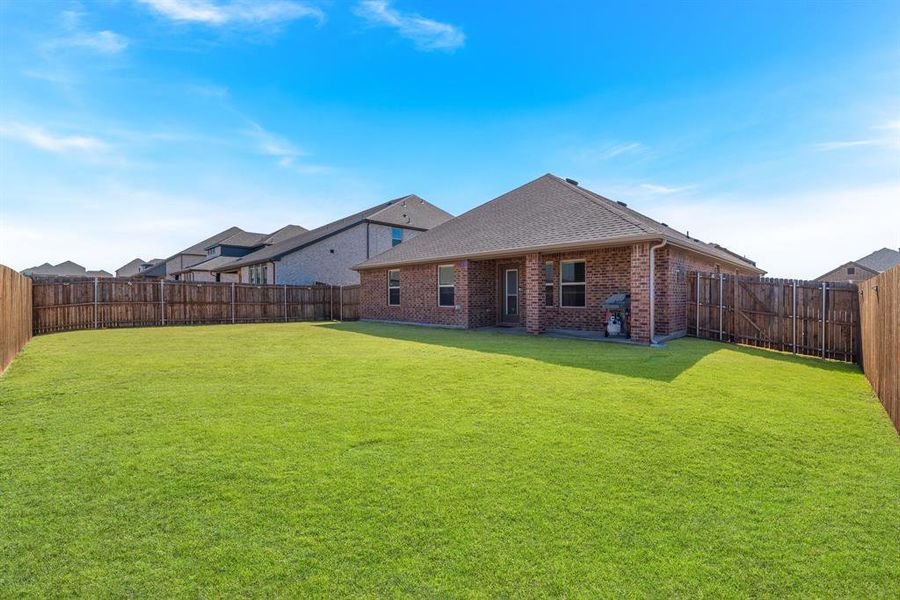 Rear view of house with a yard, a fenced backyard, a shingled roof, and brick siding