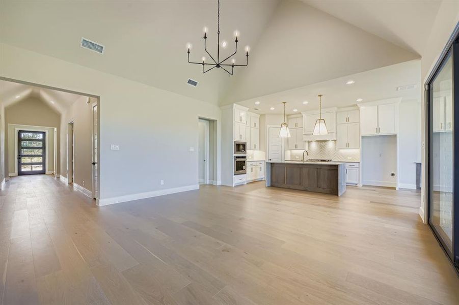 Unfurnished living room featuring a chandelier, light wood-type flooring, and high vaulted ceiling