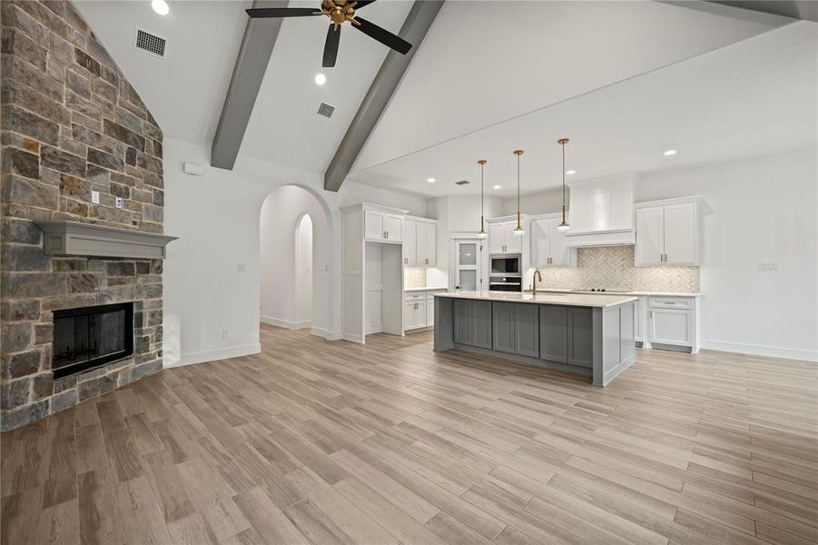 Kitchen featuring open floor plan, arched walkways, white cabinetry, a stone fireplace, and pendant lighting