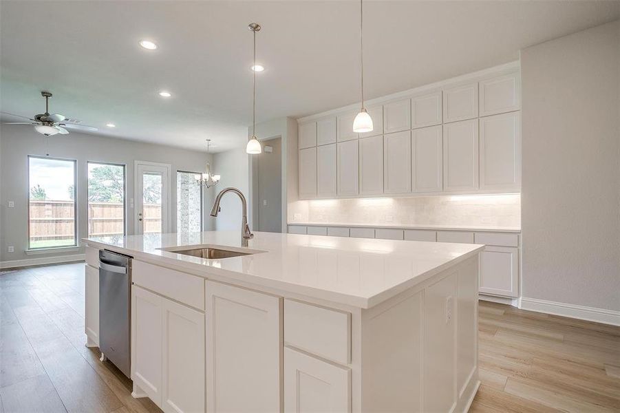 Kitchen featuring light hardwood / wood-style flooring, a center island with sink, sink, decorative backsplash, and dishwasher