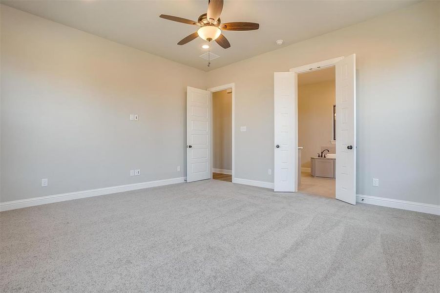 Unfurnished bedroom with light colored carpet, ensuite bathroom, and ceiling fan