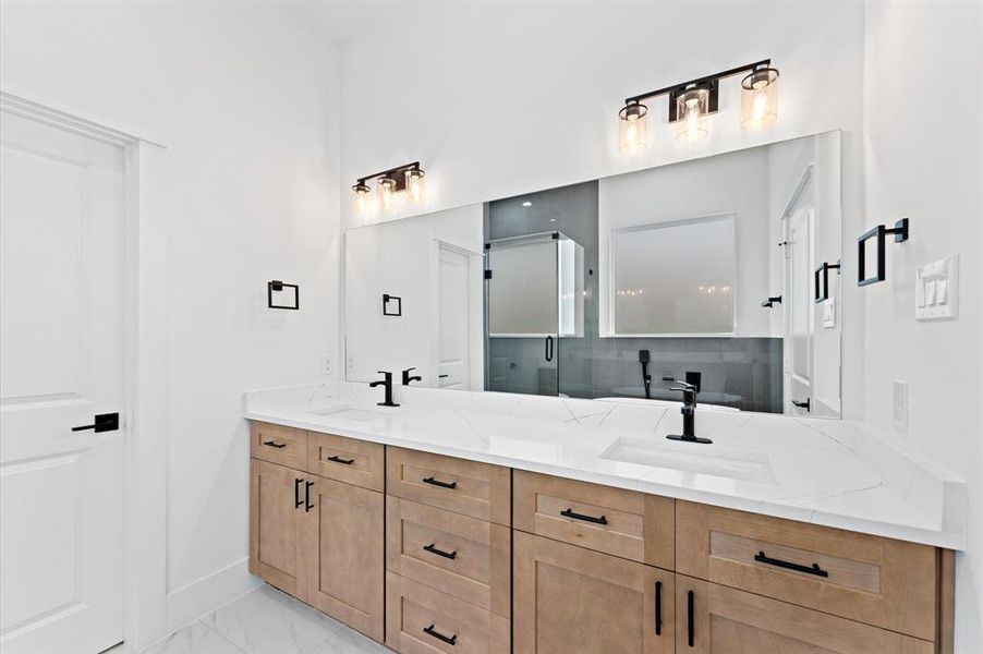 This modern bathroom features a double vanity with sleek black fixtures and ample storage. The large mirror is complemented by stylish light fixtures, while the neutral tones create a clean and inviting space.