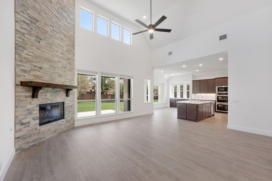 Open living area with stone fireplace, high ceilings, and open view to kitchen with dark wood cabinets