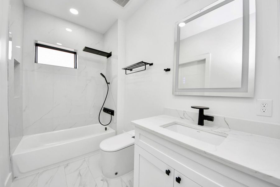 Sleek white and black secondary bathroom featuring a sizable tub, LED mirror, and a smart toilet!