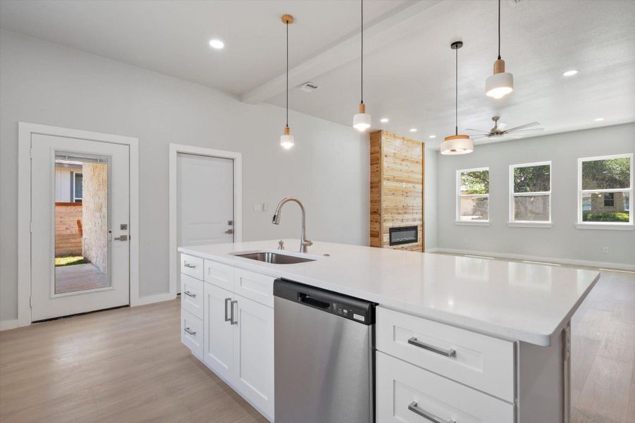A well-lit kitchen island with a sleek stainless steel dishwasher anchors this open-concept living space.