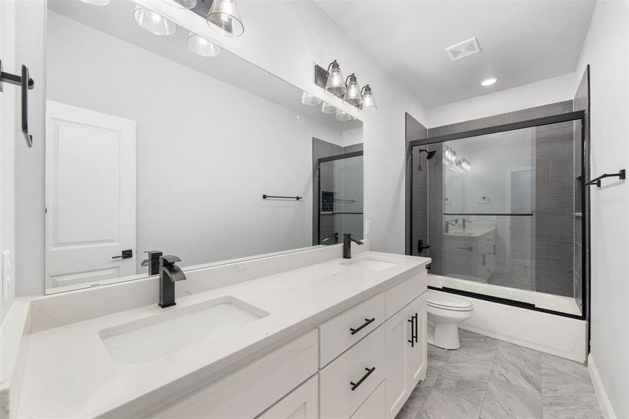 Bathroom featuring shower / bath combination with glass door, a sink, double vanity, and toilet
