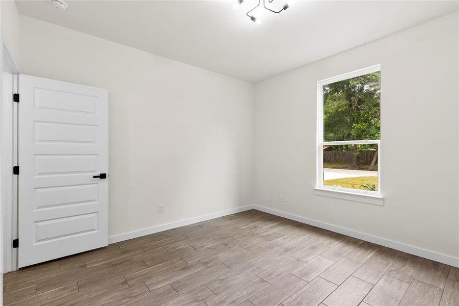 Spacious room featuring wood-finish tile flooring, white baseboards, and a single window with white trim