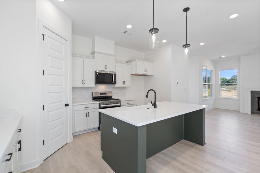 Kitchen featuring white cabinetry, center island with stone countertop and matte black faucet, stainless steel appliances, and wood-finish flooring Kitchen featuring white cabinetry, center island with stone countertop and matte black faucet, stainless steel appliances, and wood-finish flooring