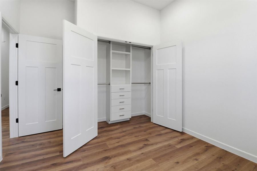 Bedroom featuring wood-finish flooring, crisp white walls, and a built-in closet system with shelving and drawers Bedroom featuring wood-finish flooring, crisp white walls, and a built-in closet system with shelving and drawers
