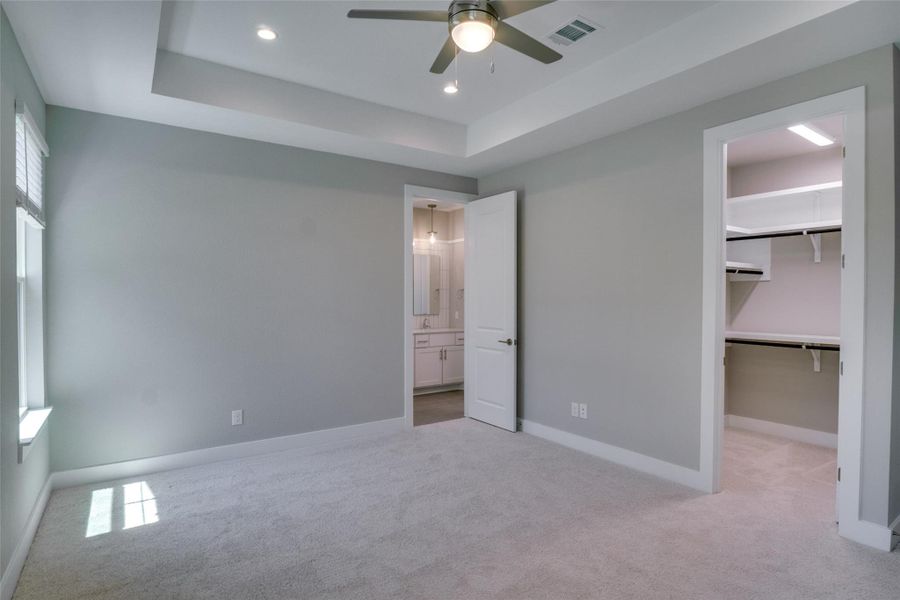 Unfurnished bedroom featuring a walk in closet, a closet, a raised ceiling, ceiling fan, and multiple windows