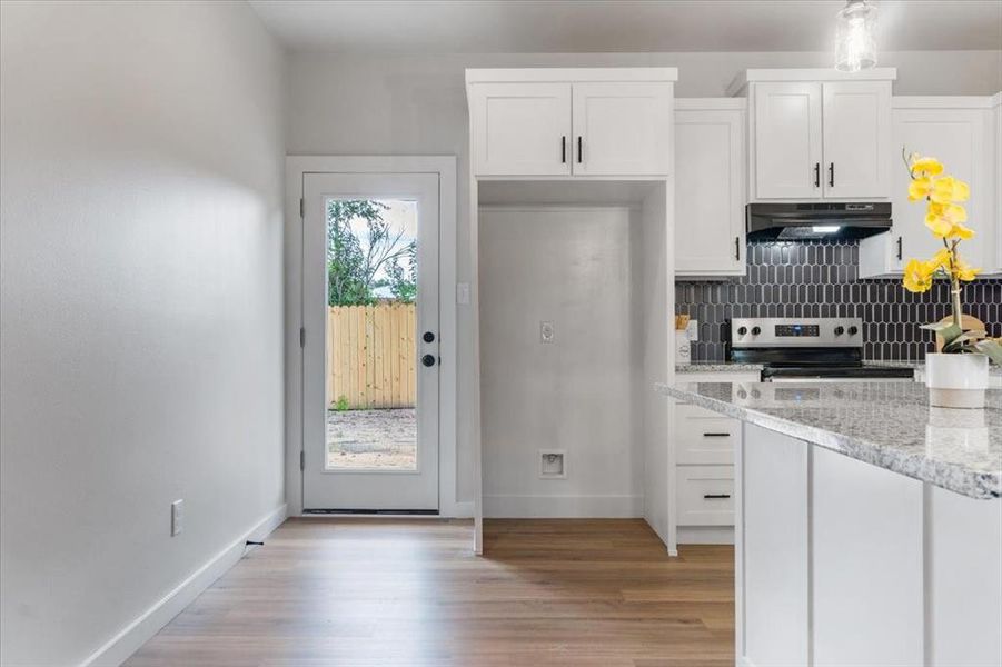 Kitchen with backsplash, white cabinetry, range, and light wood-type flooring