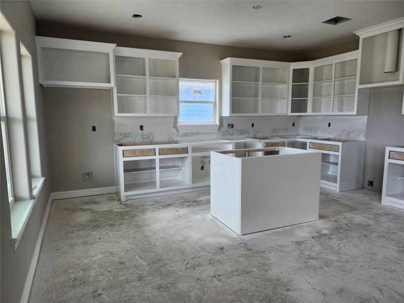 This kitchen features an open layout with white cabinetry and a central island. Large windows provide ample natural light.