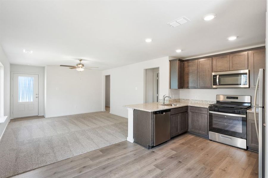 Kitchen featuring sink, appliances with stainless steel finishes, dark brown cabinetry, light stone counters, and kitchen peninsula