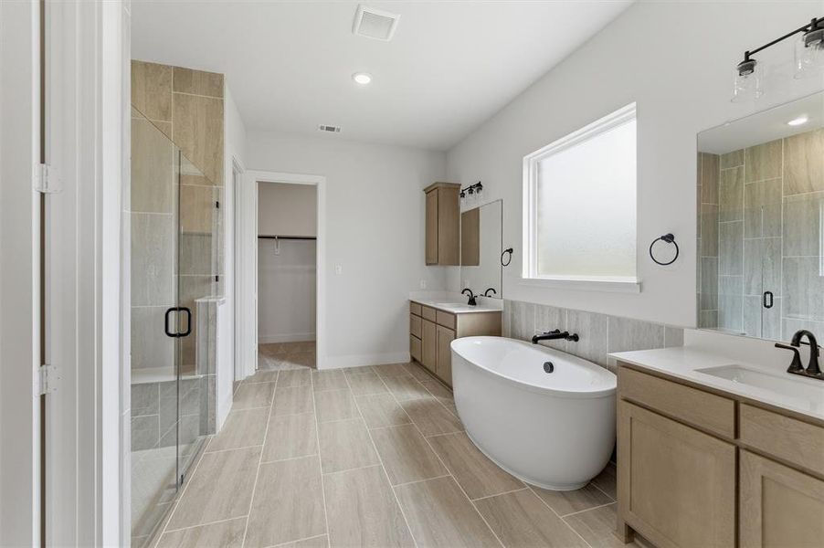 Bathroom featuring two vanities, a shower stall, a walk in closet, a freestanding tub, and recessed lighting