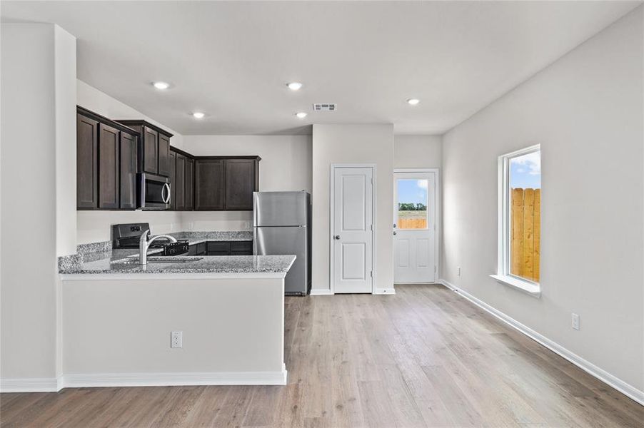 Kitchen with light stone countertops, stainless steel appliances, light wood-style flooring, recessed lighting, and a peninsula