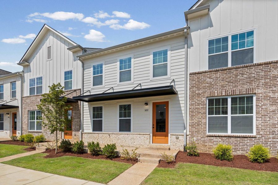 Contemporary townhome facade featuring white siding, a brick accent wall, a prominent gable, a gabled roofline, and a dark-colored awning over the entrance Contemporary townhome facade featuring white siding, a brick accent wall, a prominent gable, a gabled roofline, and a dark-colored awning over the entrance