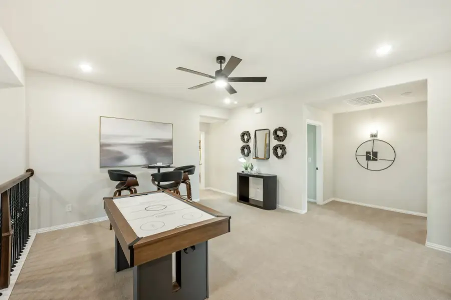 Upstairs game room with air hockey table, ceiling fan, and carpet flooring near staircase railing