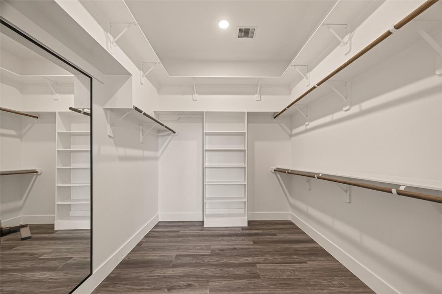 Spacious walk-in closet with ample shelving and hanging space, featuring elegant wood flooring and a large mirror for convenience. Spacious walk-in closet with ample shelving and hanging space, featuring elegant wood flooring and a large mirror for convenience.
