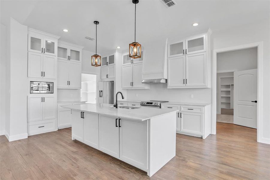 Kitchen featuring white cabinetry, light hardwood / wood-style flooring, an island with sink, appliances with stainless steel finishes, and sink