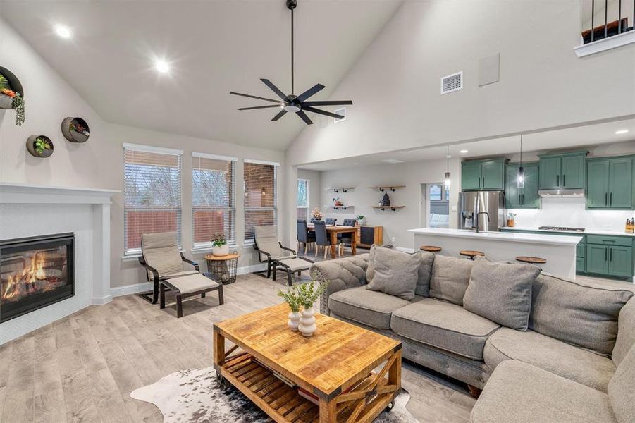 Living area featuring recessed lighting, vaulted ceiling, light wood-style floors, a glass covered fireplace, and a ceiling fan