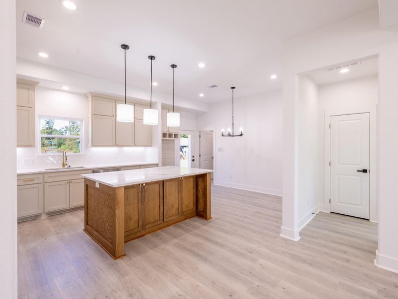 This photo showcases a modern, open-concept kitchen with a large island featuring a wood base and white countertop. The kitchen is bright, with recessed lighting and pendant lights above the island. It has light wood flooring and ample cabinetry, creating a spacious and inviting atmosphere.