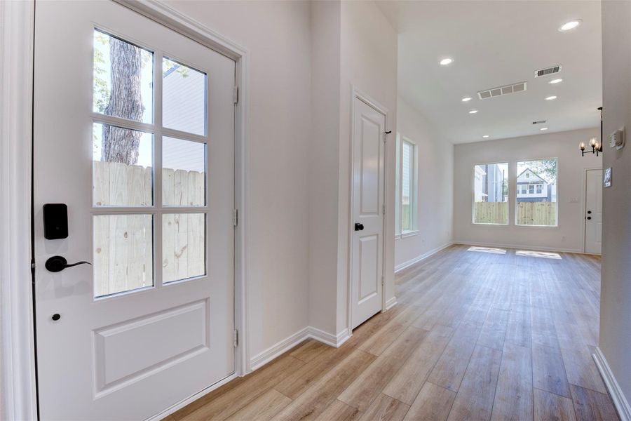 Welcoming entry with a glass-paneled front door that brings in natural light while maintaining privacy. Wood-look LVP flooring flows throughout, paired with tall ceilings and a clean, neutral palette.