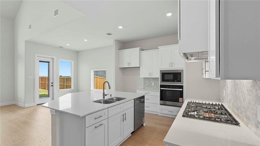 Kitchen featuring a kitchen island with sink, white cabinetry, stainless steel appliances, decorative backsplash, and light wood finished floors