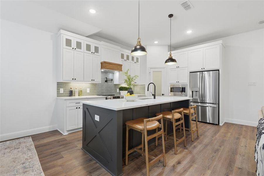 Two tone kitchen with two tone cabinetry, stainless steel appliances, a center island with sink, a kitchen bar, and dark wood-style flooring