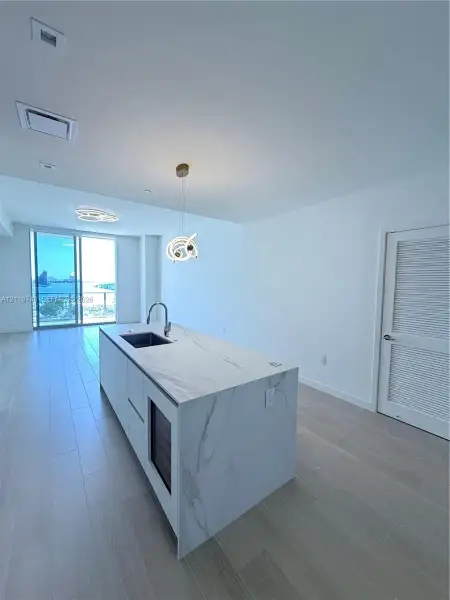 Kitchen island with stone-finish waterfall countertop, undermount sink, built-in wine cooler, and high-arc faucet, complemented by wood-finish flooring and floor-to-ceiling glass panel door