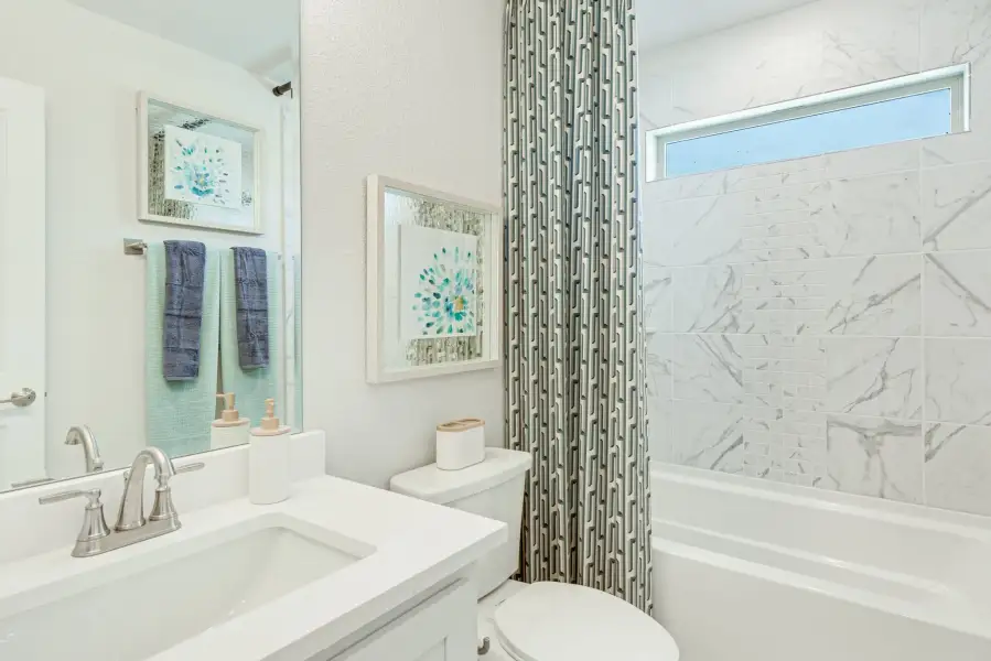 Bathroom with white vanity, marble-tiled tub surround, patterned shower curtain, and small window above the tub
