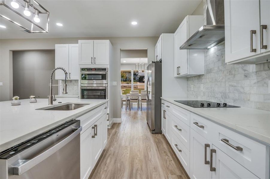 Kitchen featuring stainless steel appliances, white cabinetry, wall chimney range hood, light stone countertops, and light wood-style floors