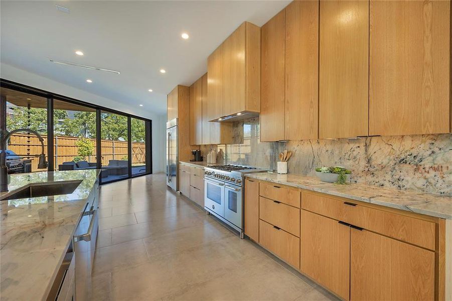 Kitchen with light stone countertops, premium appliances, tasteful backsplash, sink, and range hood