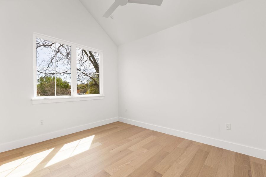 Spare room featuring light wood-style flooring, vaulted ceiling, and a ceiling fan