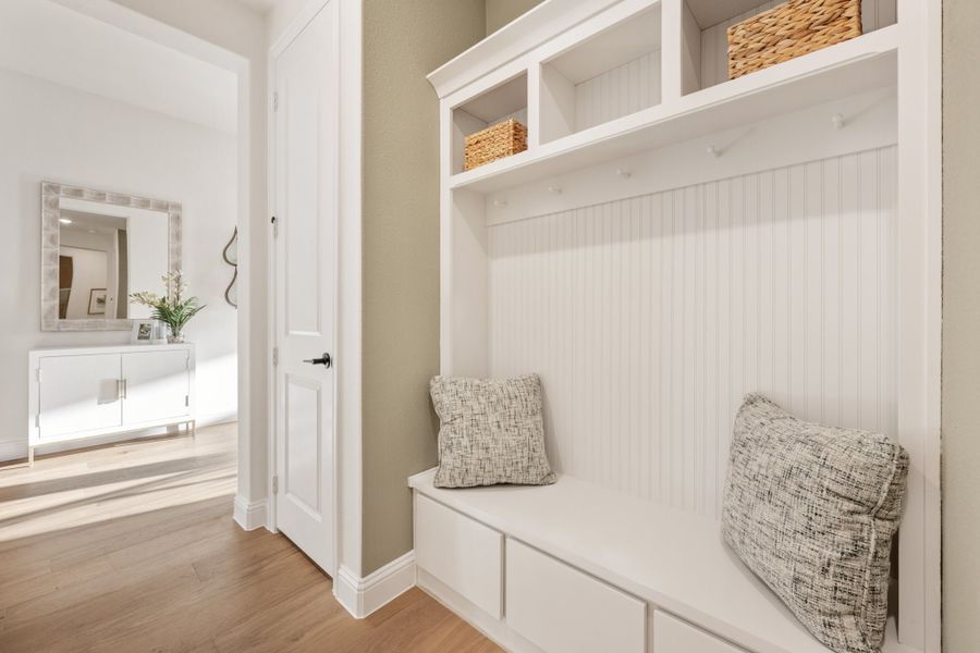 White built-in mudroom with bench seating, coat hooks, open shelves, and wicker baskets on hardwood floors