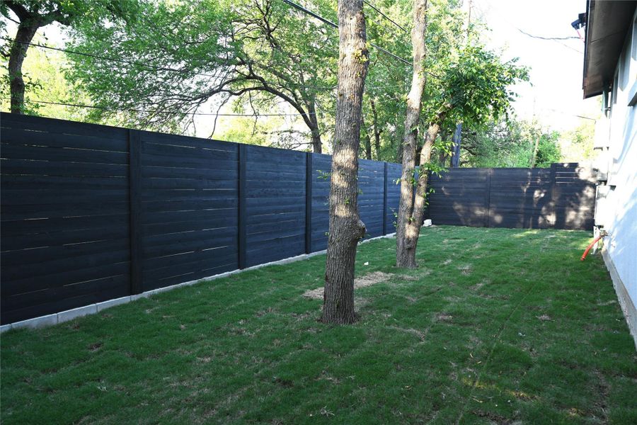 The backyard features a well-maintained lawn, mature trees, and a dark-toned privacy fence