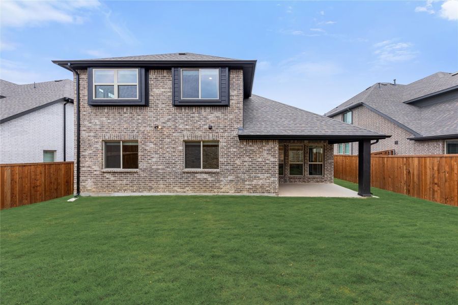 Two-story brick home rear exterior with covered patio, green lawn, and wood privacy fence Two-story brick home rear exterior with covered patio, green lawn, and wood privacy fence
